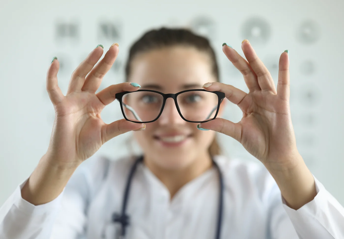 Unrecognizable female doctor correcting ophthalmic glasses selecting lenses on eyes of female patient during appointment in clinic against white wall